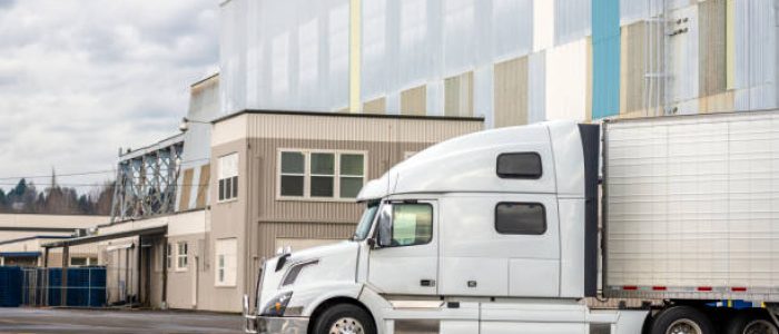 White big rig long haul semi truck with high cab and reefer semi trailer standing on parking lot waiting for loading and possibility of continuing to the destination according to approved schedule